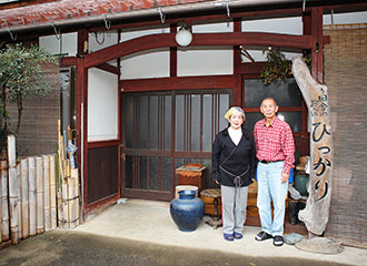 写真：農家民宿「ぴっかり」の玄関に立つ西田さん夫婦