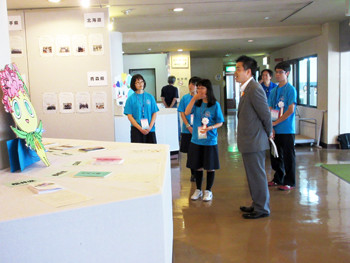 三日月知事が今津東コミュニティセンターへ立ち寄り、県内高校生から展示されている文芸部誌の説明を受けている様子。