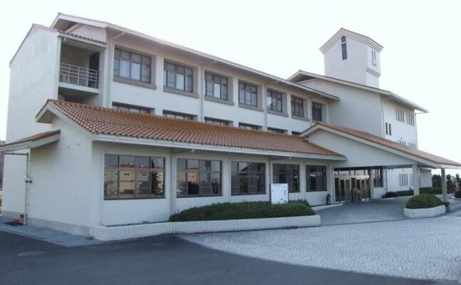 白い壁で赤茶色の洋風屋根の3階建ての建物。