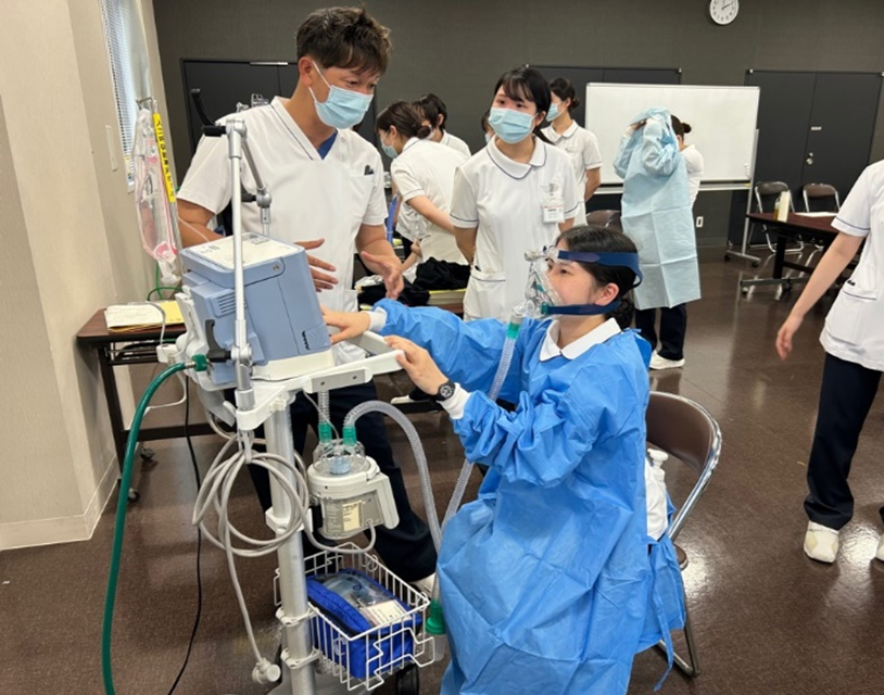 人工呼吸器を装着し椅子に着席し機器を操作する演習風景