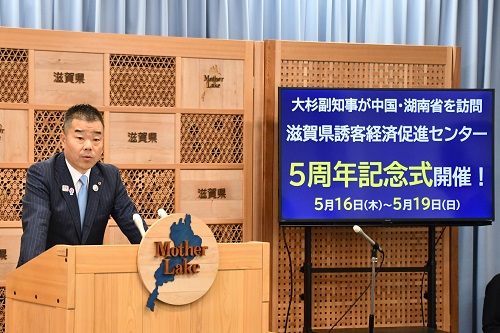 知事定例会見にて壇上で話す三日月知事の写真。本日の話題提供の情報がモニターに表示されている。