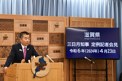 知事定例会見にて壇上で話す三日月知事の写真。知事の横に大きなモニターが映っている。モニターには三日月知事定例記者会見令和6年(2024年)4月23日と書かれた画面が表示されている。